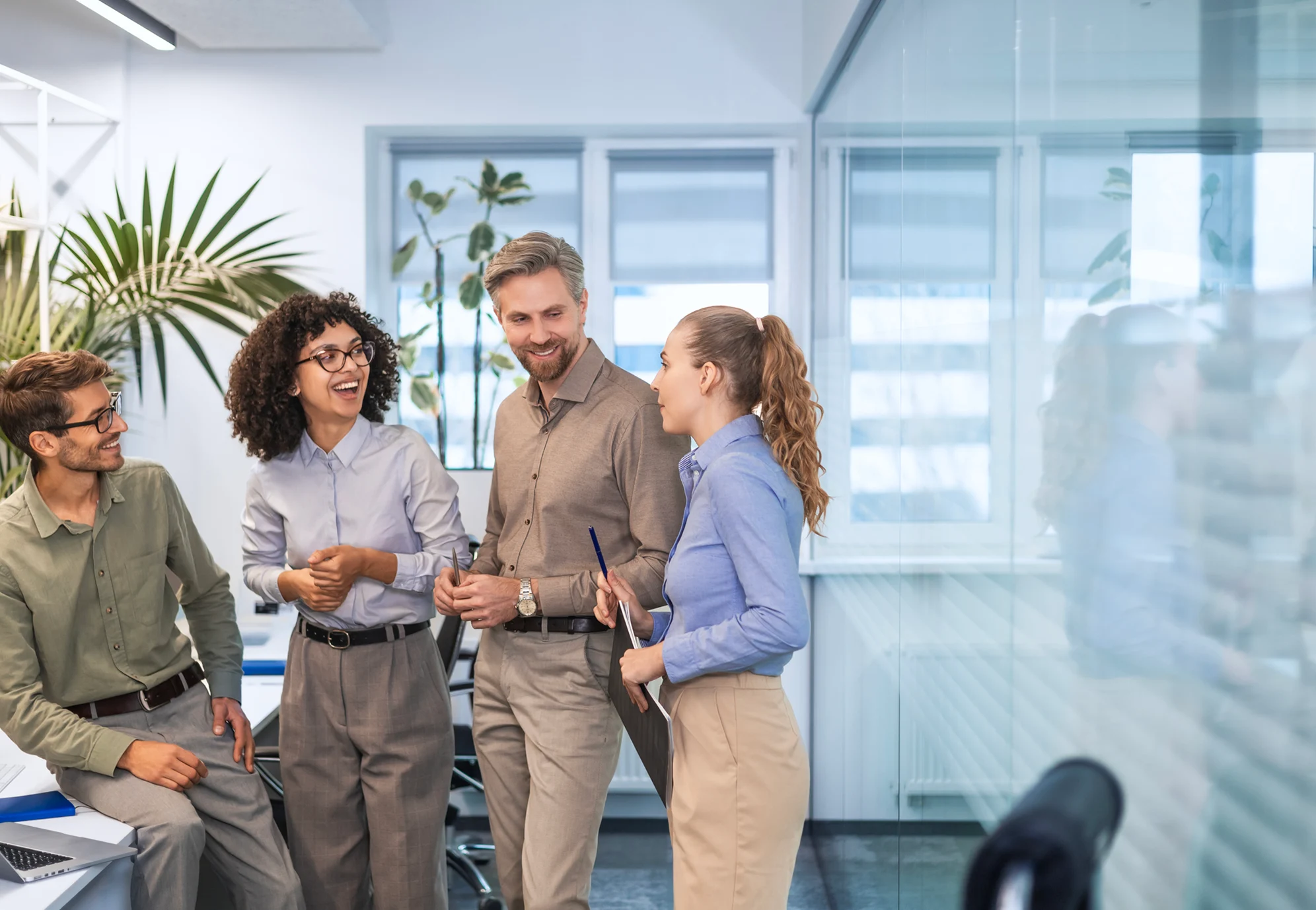 Three colleagues smiling and discussing work in a modern office.
